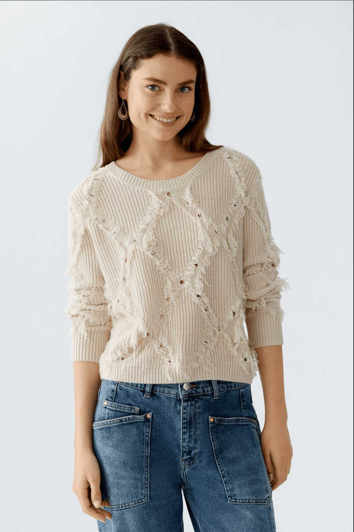 Tricot motif losange avec franges et détails métalliques, coupe courte, col ras du cou, porté avec jean taille haute.