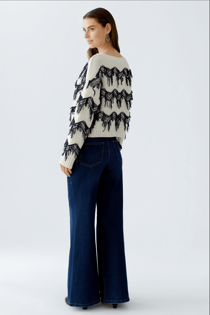 Femme portant un tricot motif zigzag avec franges tricotées et coupe carrée.