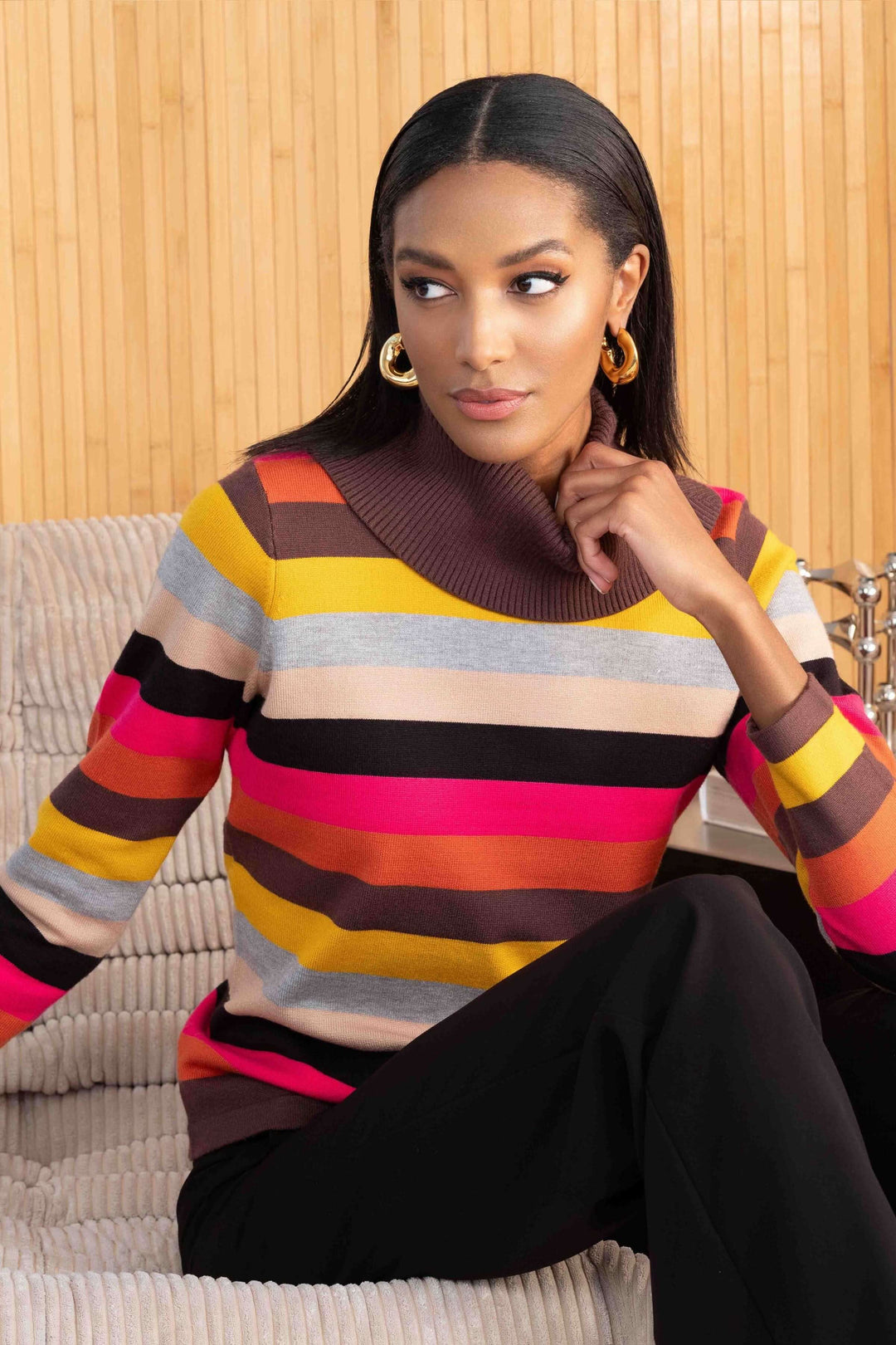 Tricot rayures multi à col roulé souple avec rayures multicolores, porté par une femme assise dans un cadre moderne.