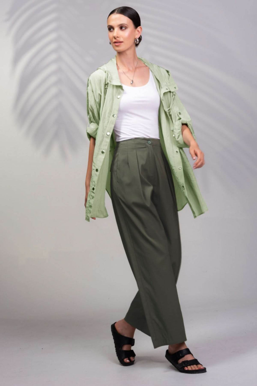 Femme portant une veste à capuche surdimensionnée verte, un débardeur blanc et un pantalon large, style décontracté.