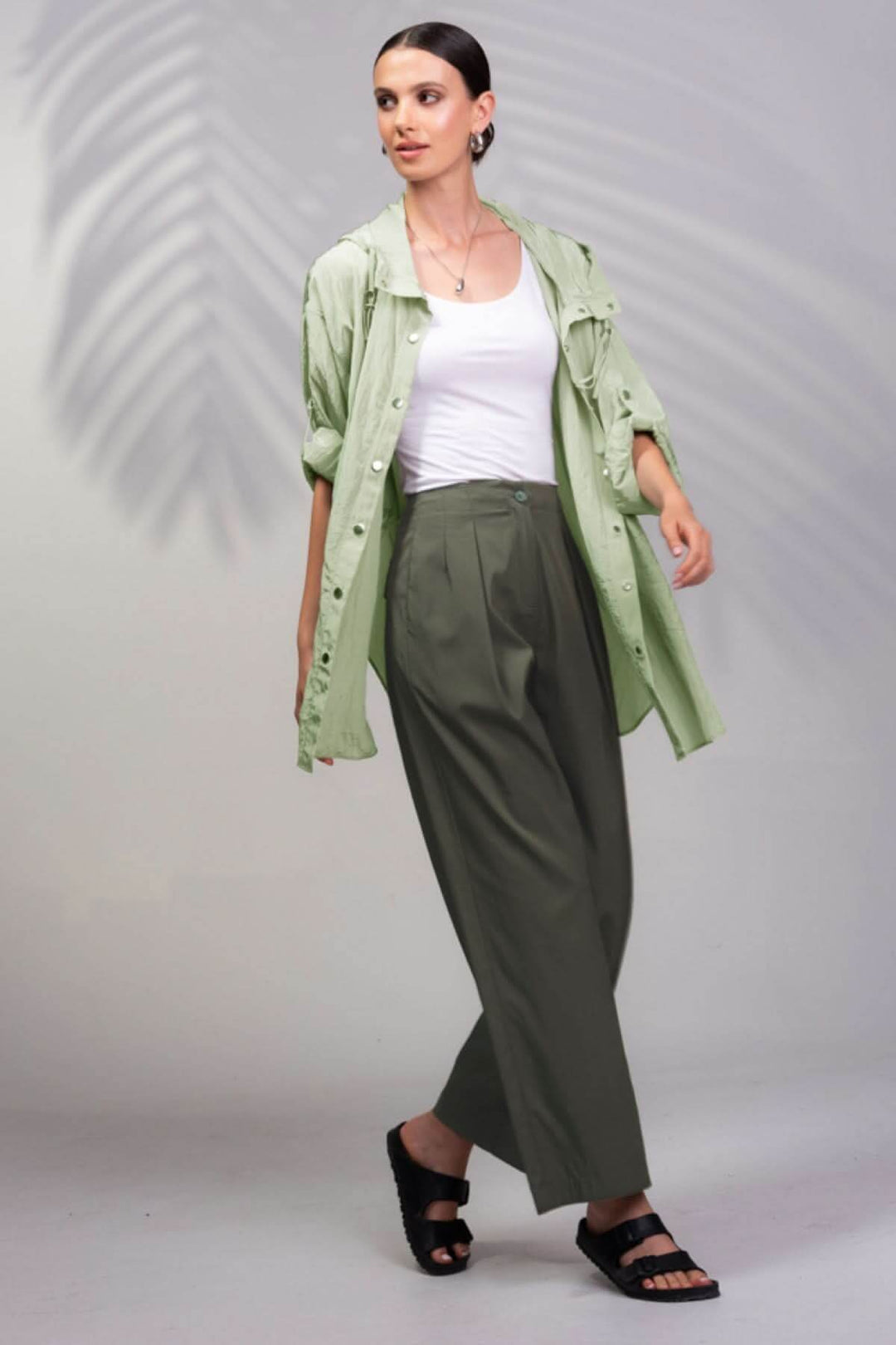 Femme portant une veste à capuche surdimensionnée verte, un débardeur blanc et un pantalon large, style décontracté.