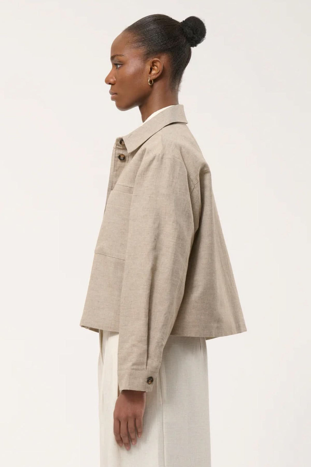 Veste chemise courte beige avec col chemise et poches plaquées, vue de côté sur mannequin, style élégant et décontracté.