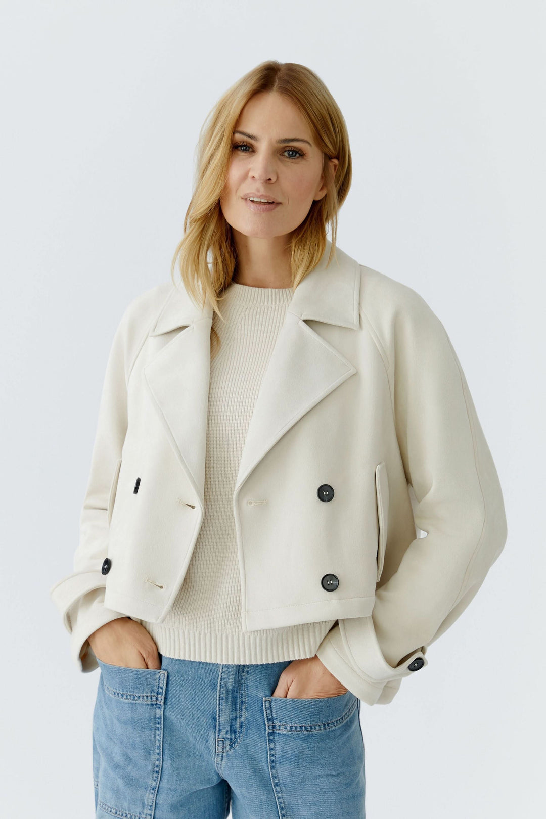 Veste courte croisée à col tailleur sur femme portant un chandail beige et jean, style moderne et élégant.