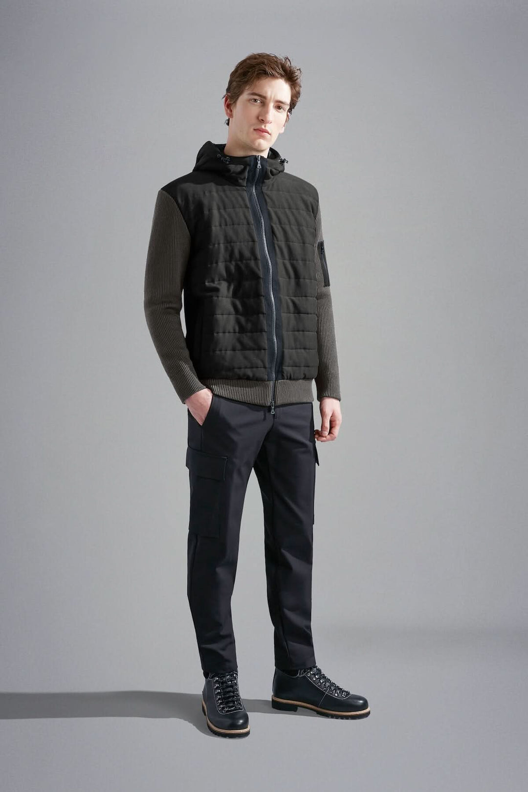 Homme portant une veste imperméable à capuchon, style hybride, avec matelassage et manches en tricot.