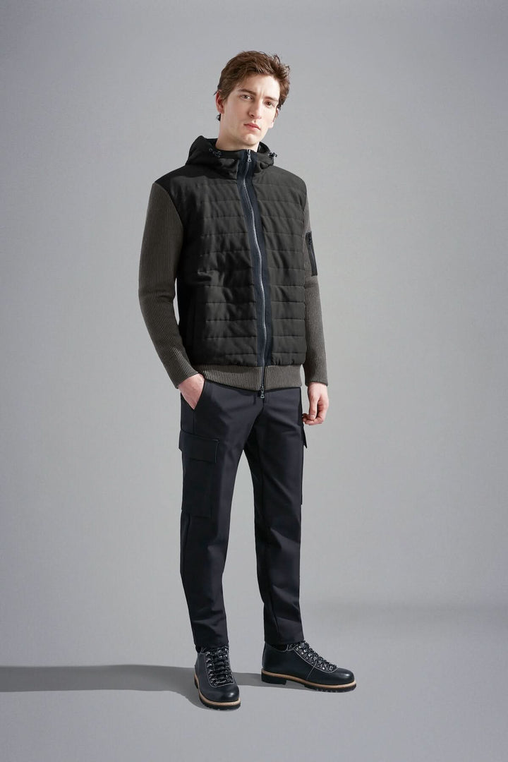 Homme portant une veste imperméable à capuchon, style hybride, avec matelassage et manches en tricot.
