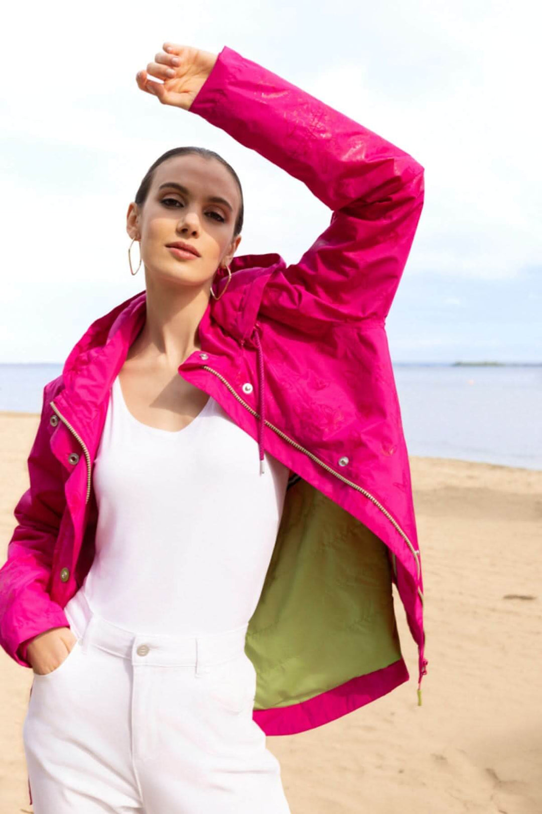 Femme portant une veste légère à capuche rose vif sur la plage.