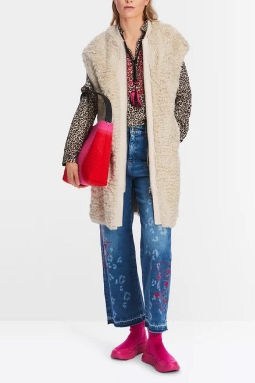 Femme portant une veste longue en fourrure bouclée, avec un look décontracté, jeans amples et bottines rose.