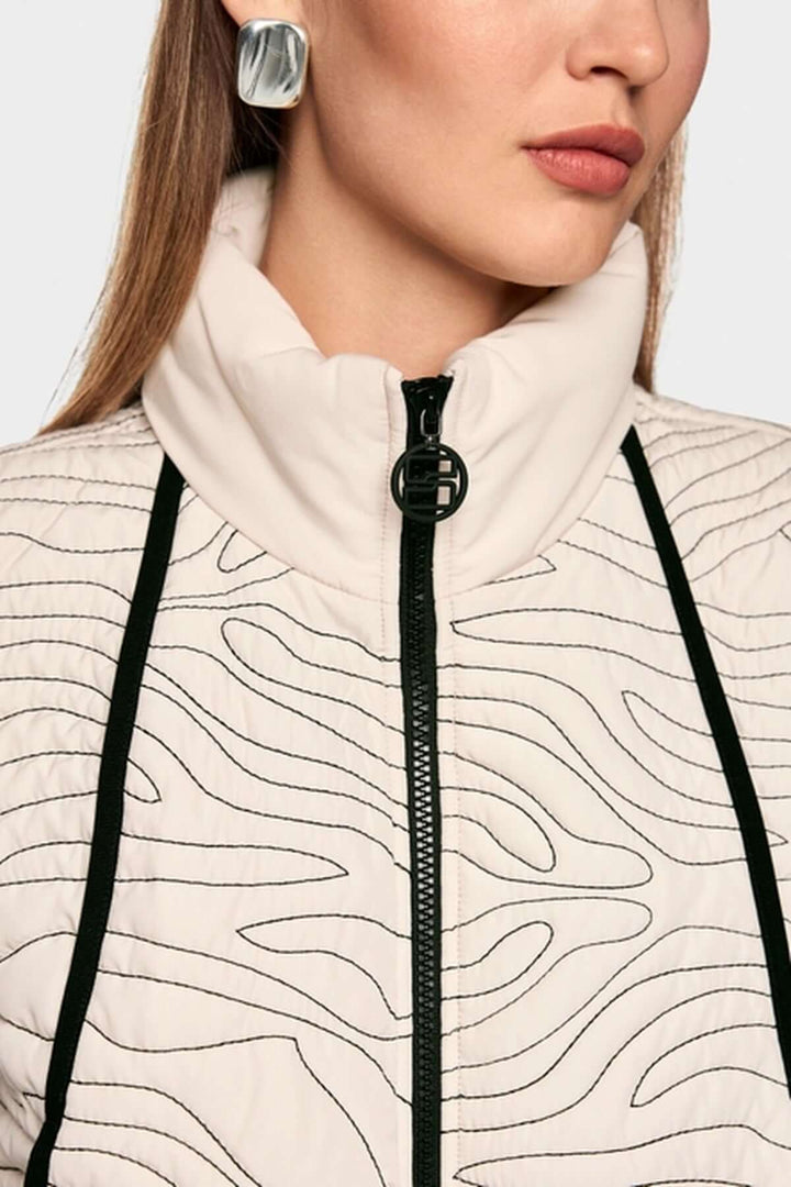 Veste matelassée avec surpiqûres ondulées et col montant, ceinture élastique, fermeture éclair et poches latérales visibles.