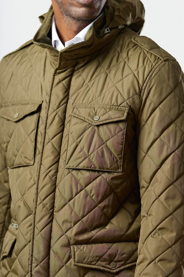 Homme portant une veste matelassée à capuche escamotable avec matelassage losange et poches utilitaires.
