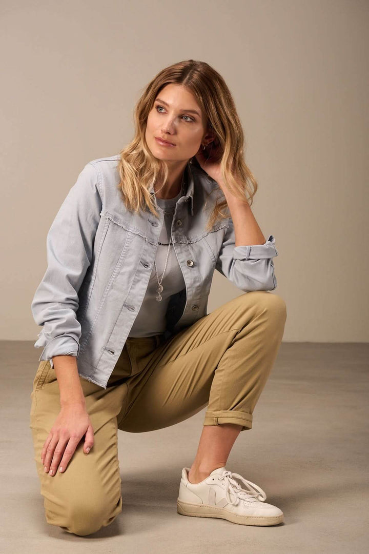 Femme en veste sportive décontractée, assise avec des pantalons beige et baskets blanches, look casual moderne.