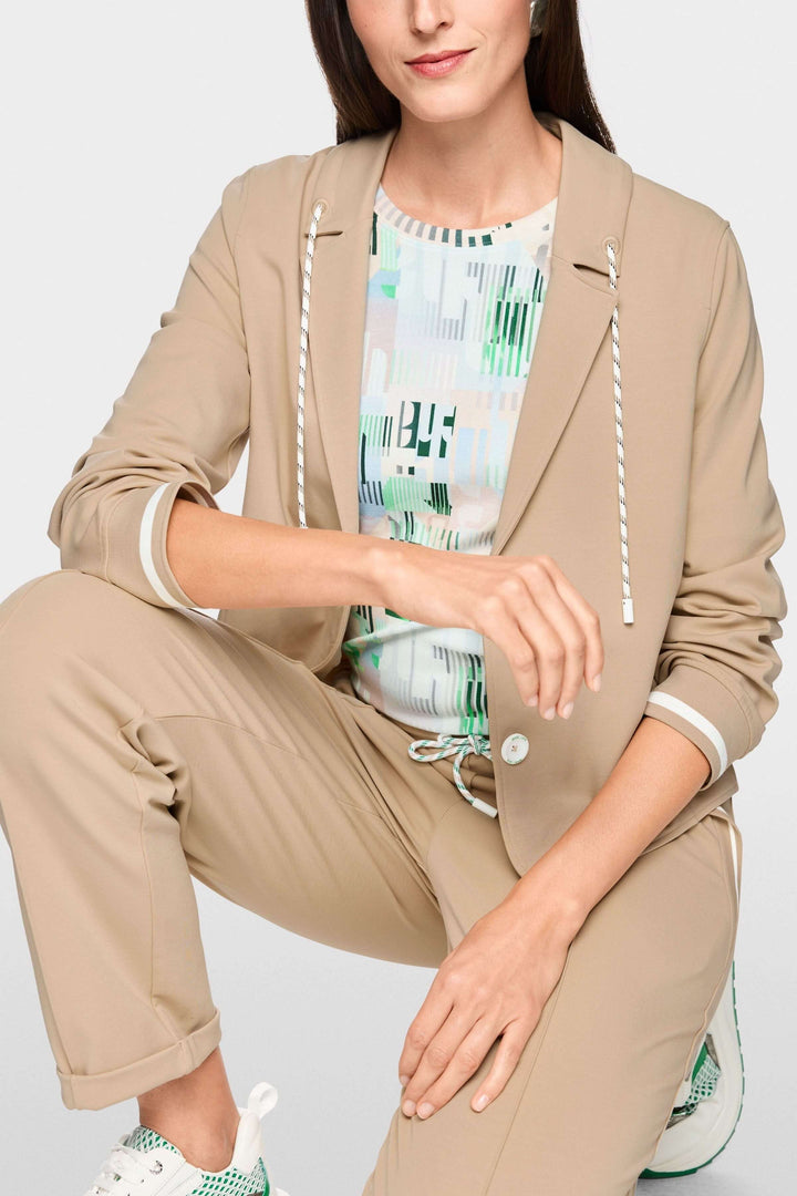 Veston sportif à détails rayés porté avec t-shirt imprimé et pantalon beige, coupe moderne et élégante avec capuchon à cordon.