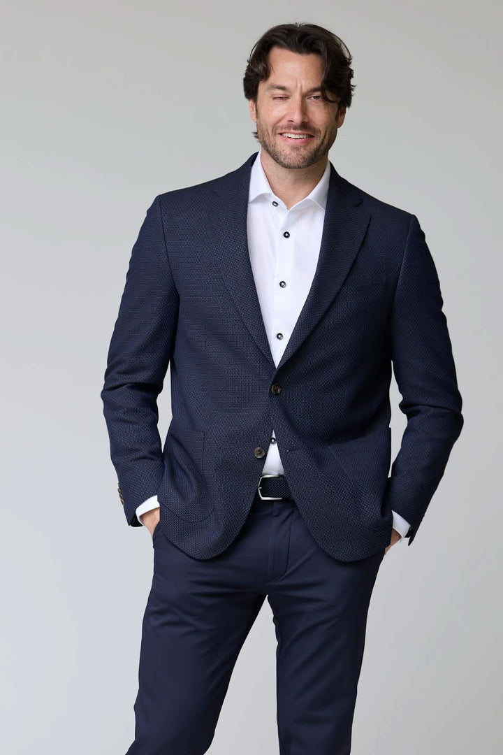 Homme portant un veston texturé à coupe moderne, bleu marine, avec chemise blanche et pantalon assorti, style élégant et contemporain.