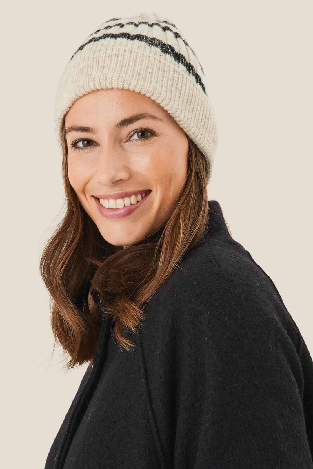 Femme souriante portant un bonnet à rayures grises, en laine et coton, avec une veste noire.