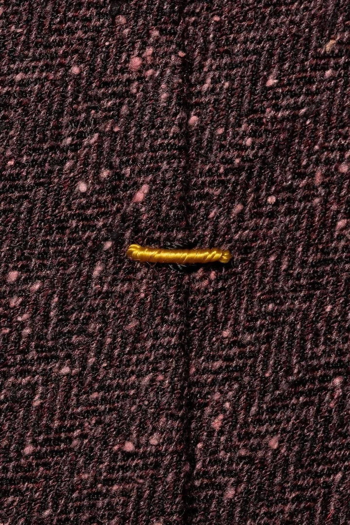 Détail du tissu en laine bordeaux avec un bouton doré sur un fond texturé.