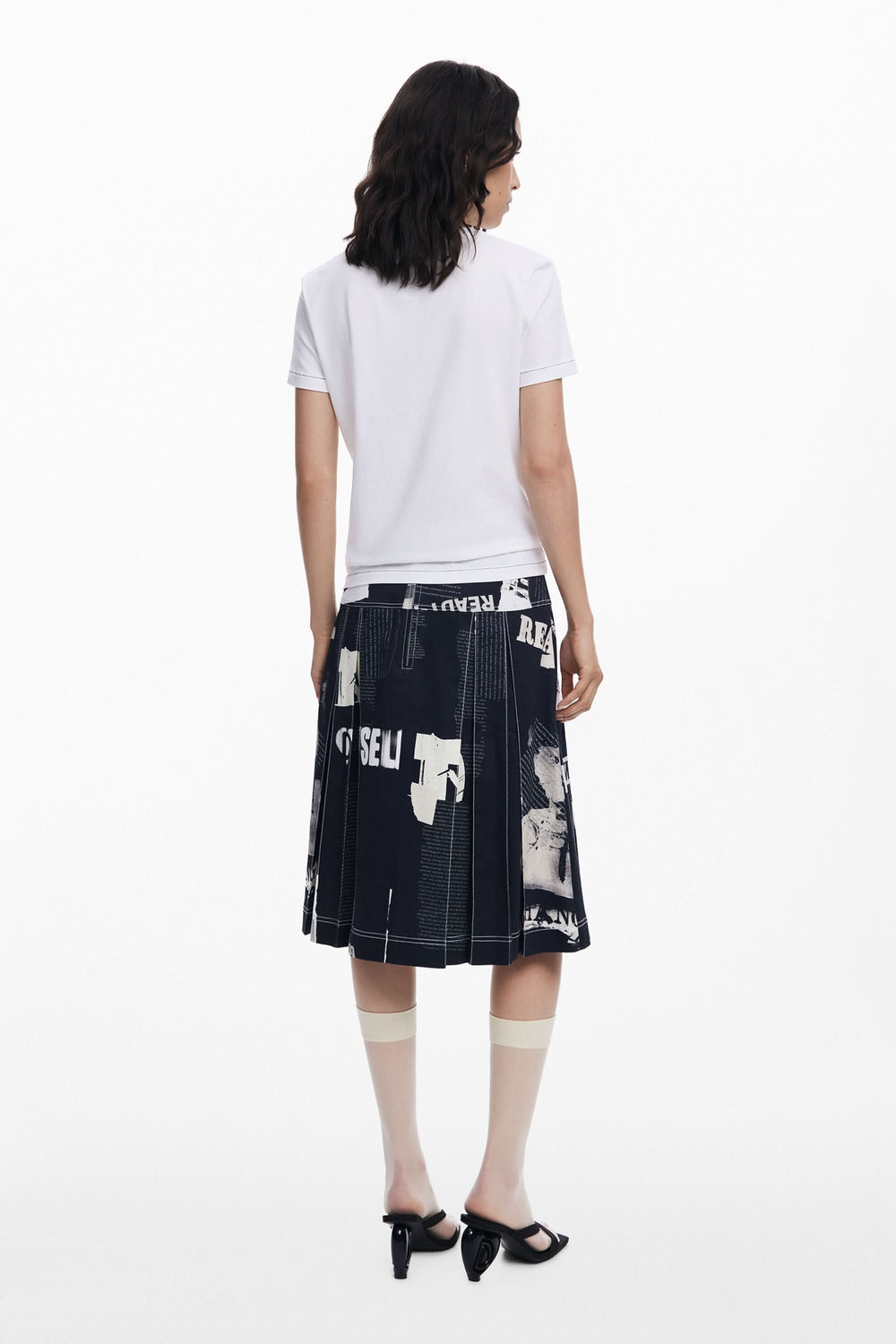 Femme vue de dos portant un t-shirt blanc et une jupe en denim à motifs, style moderne et engagé.