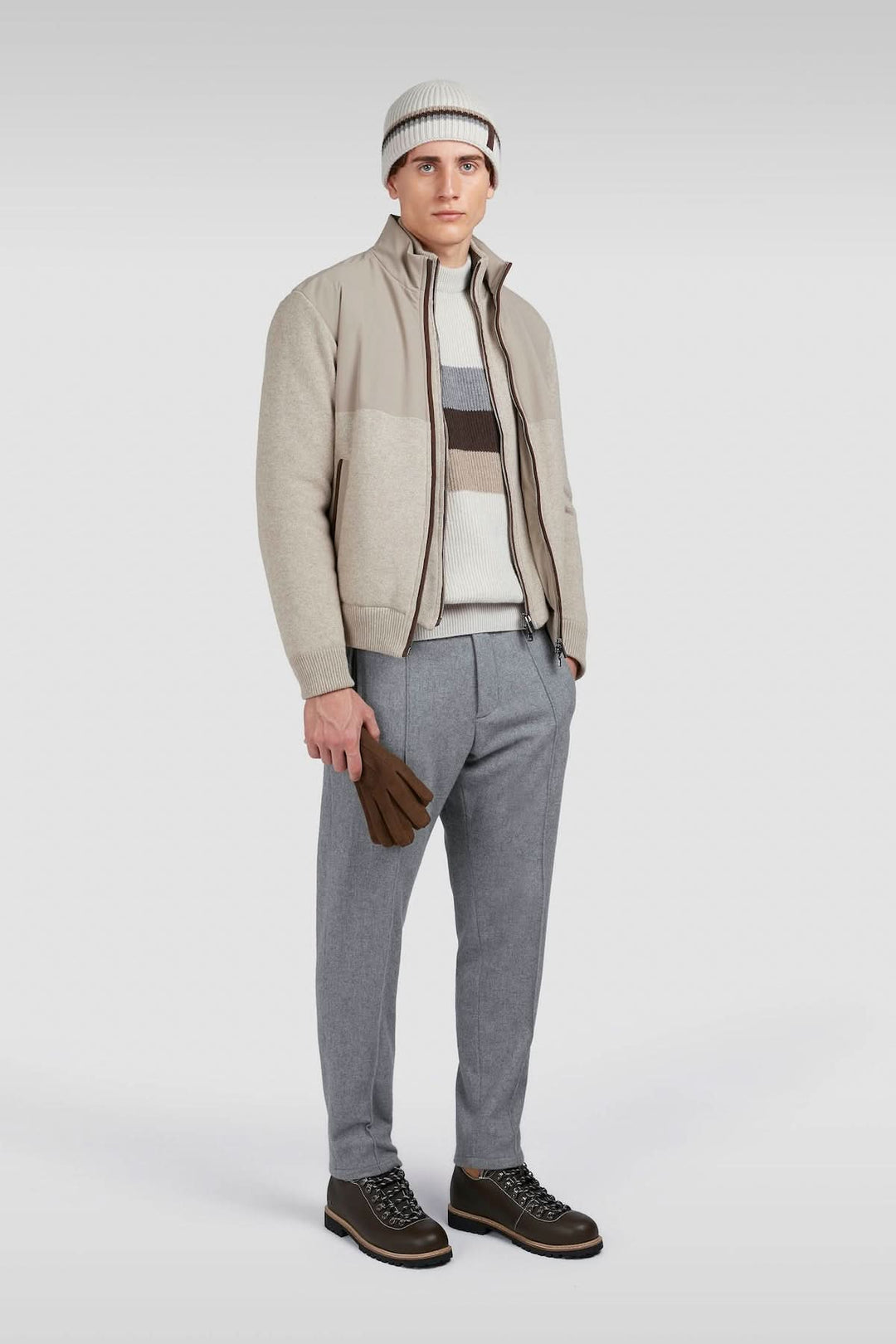 Homme en tenue décontractée, portant une veste beige, pantalon gris, et accessoires assortis, style moderne.