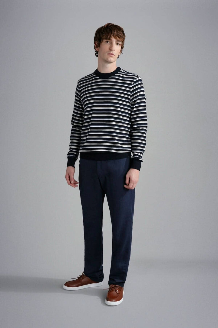 Homme portant un chandail rayé noir et blanc avec un pantalon bleu marine et des chaussures marron.