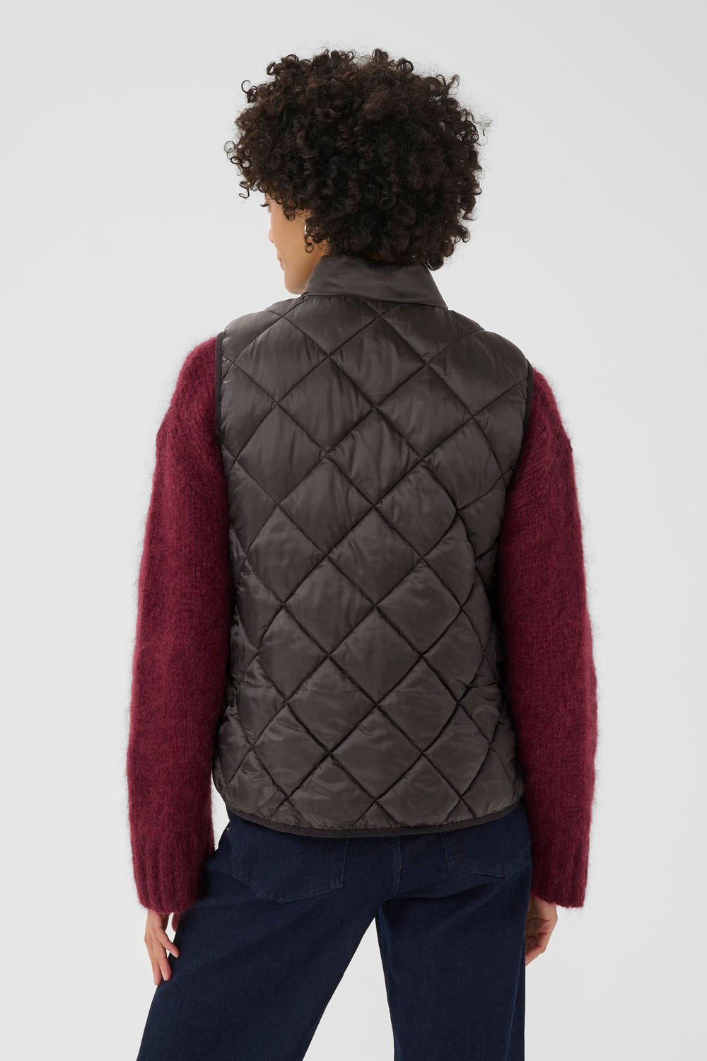 Femme portant un manteau sans manches matelassé noir avec un pull bordeaux, vue de dos, style moderne et décontracté.