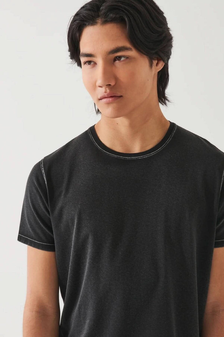 Homme portant un t-shirt stretch vintage wash en coton pima noir, avec couture contrastante.