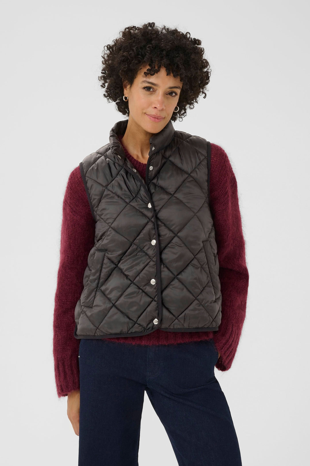 Manteau sans manches matelassé Sidse pour une allure moderne et décontractée, porté sur un chandail rouge.