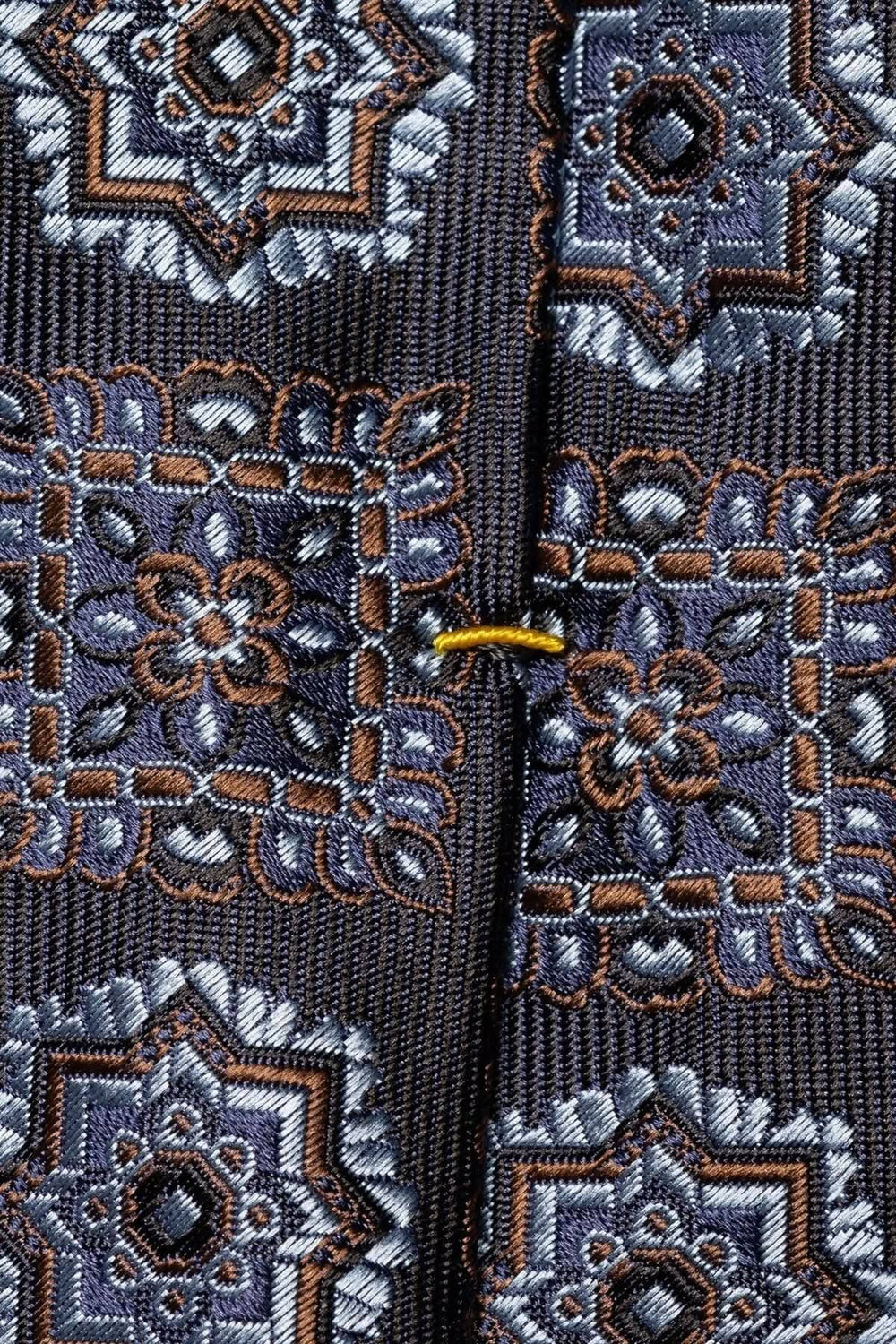 Détail d'une cravate en soie avec motif médaillon en nuances de bleu, brun et blanc.