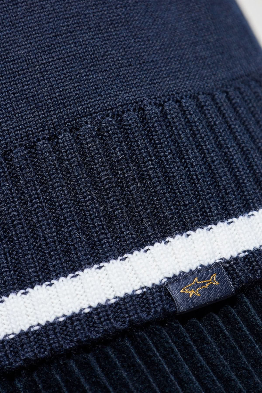 Chapeau en tricot bleu marine avec bande blanche et étiquette brodée, parfait pour les journées fraîches.