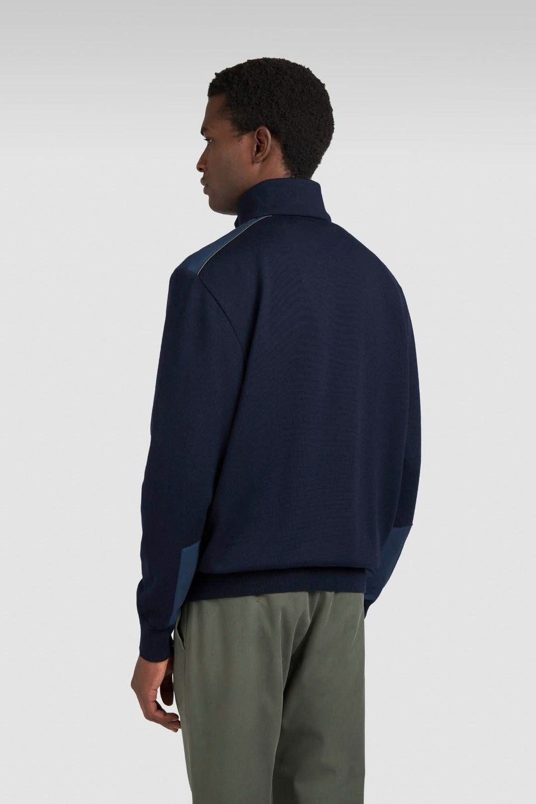 Homme portant un chandail en tricot bleu à col zippé, vue de dos, avec empiècements contrastants.