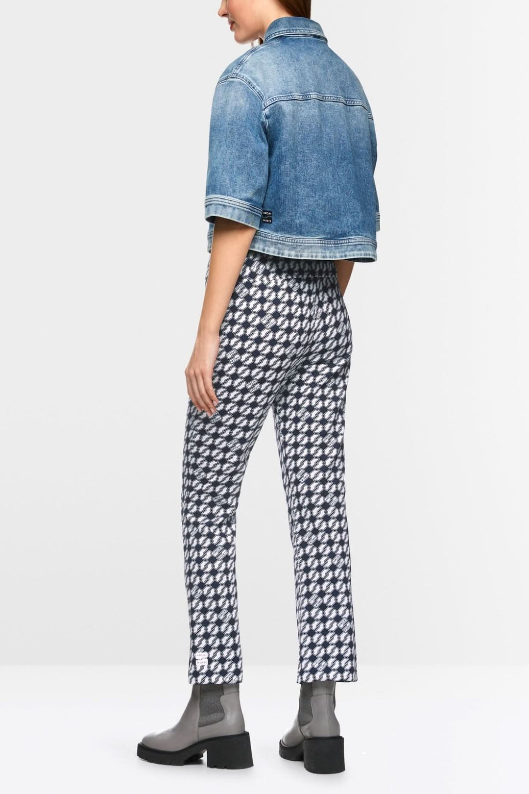 Femme de dos portant un pantalon FREDERICA imprimé Cube, associé à une veste en jean et des bottines noires.