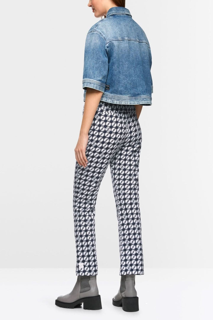 Femme de dos portant un pantalon FREDERICA imprimé Cube, associé à une veste en jean et des bottines noires.