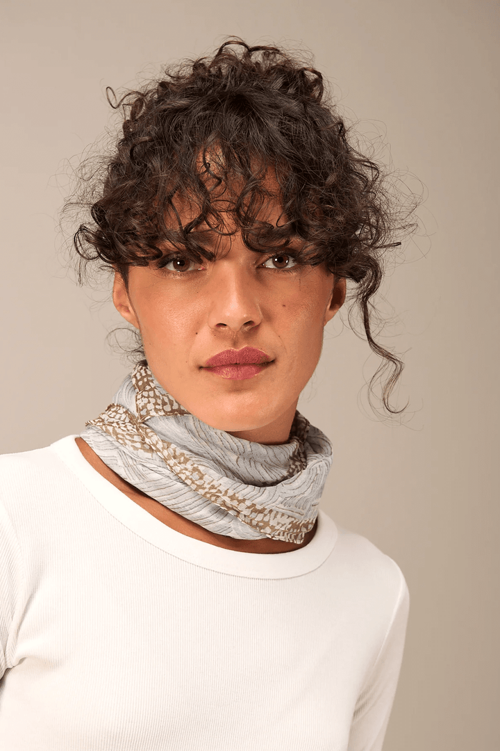Femme portant un foulard imprimé léger et fluide, accessoire de mode élégant autour du cou avec motif subtil.