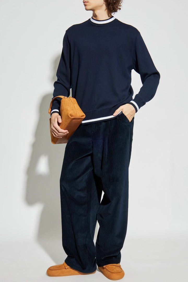 Homme portant un chandail col rond avec bandes contrastantes, pantalon ample et accessoires modernes.