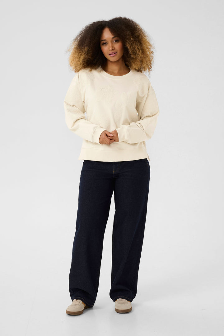 Coton ouaté Josie beige avec broderies florales, porté sur un pantalon noir pour un look chic et décontracté.