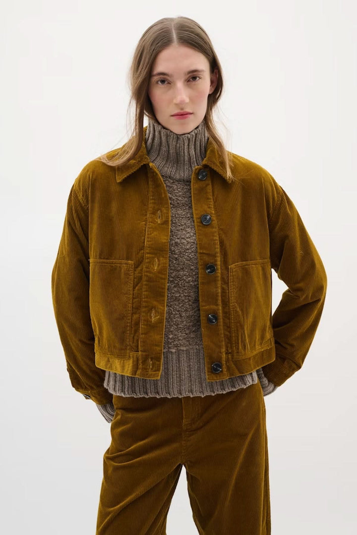 Veste en velours côtelé brune avec col chemise, portée sur un pull gris, pour un look rétro tendance.
