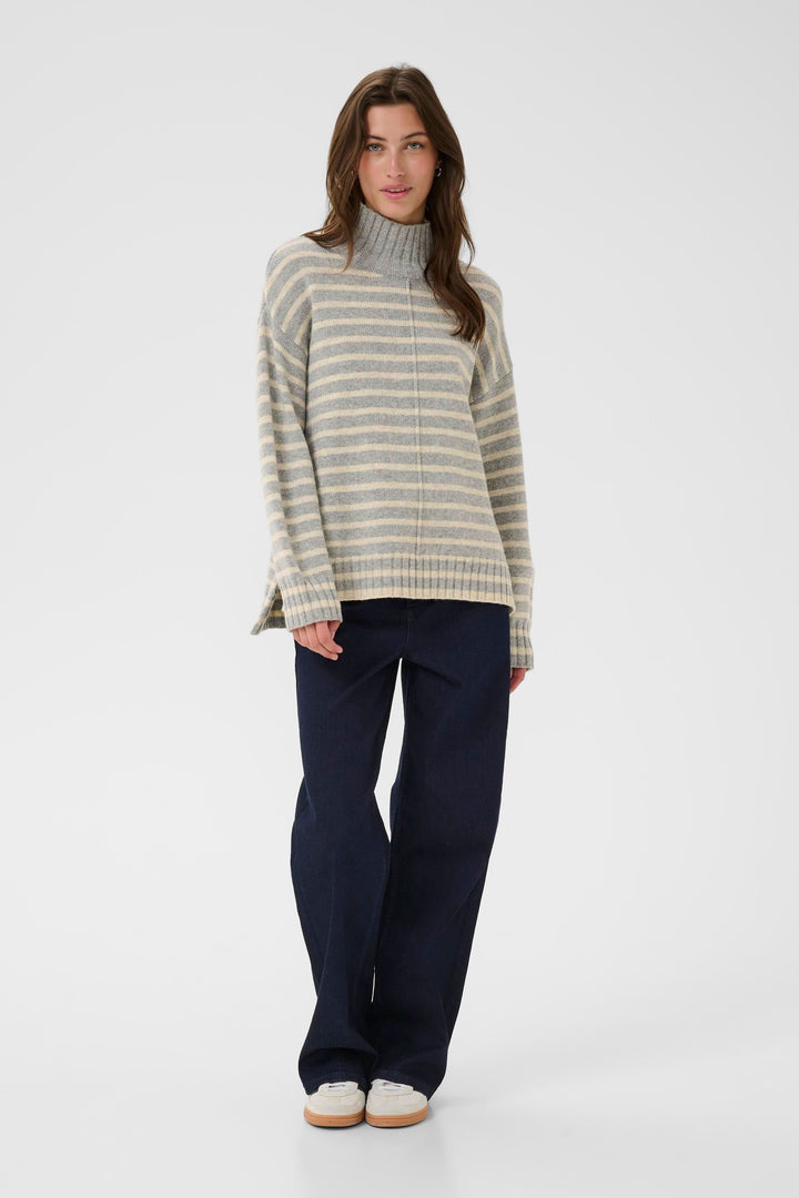 Tricot à col montant avec rayures horizontales, coupe ample, porté avec un jean foncé pour un look décontracté et élégant.