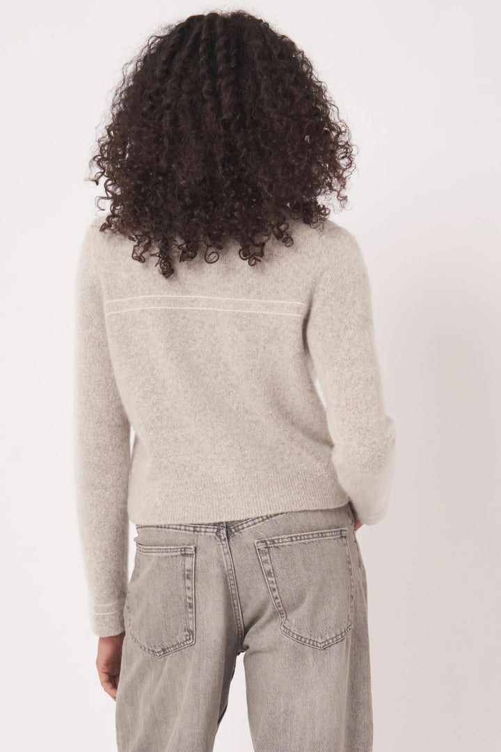 Cardigan en maille beige avec poches plaquées vu de dos, porté avec jeans pour une allure élégante et décontractée.