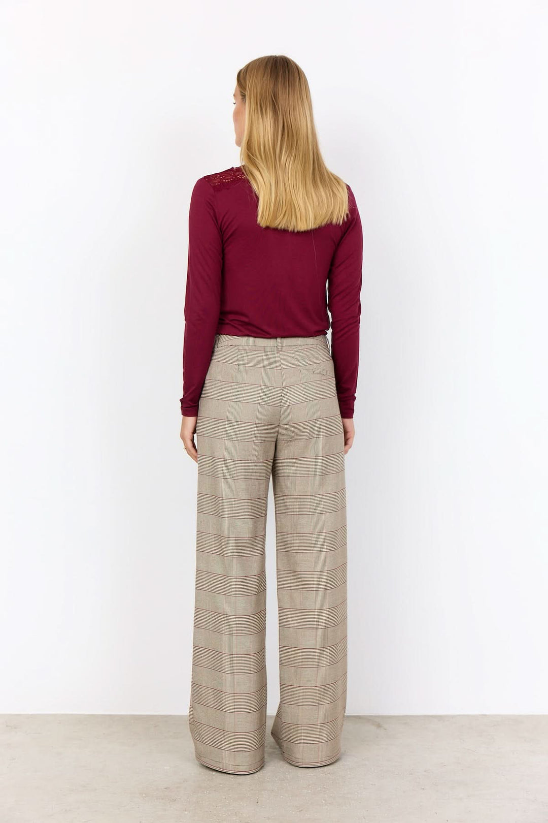 Femme vue de dos portant un pantalon à carreaux large avec un haut ajusté rouge.