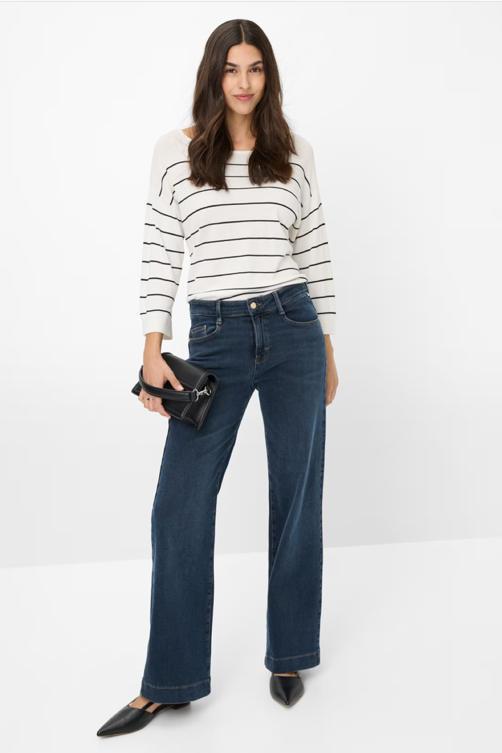 Femme portant un jean délavé évasé avec un pull rayé, accessoirisé d'un sac à main noir.