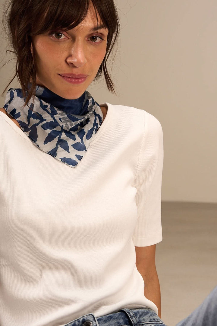 Foulard carré imprimé feuillage porté par une femme, ajoutant une touche élégante à une tenue simple.
