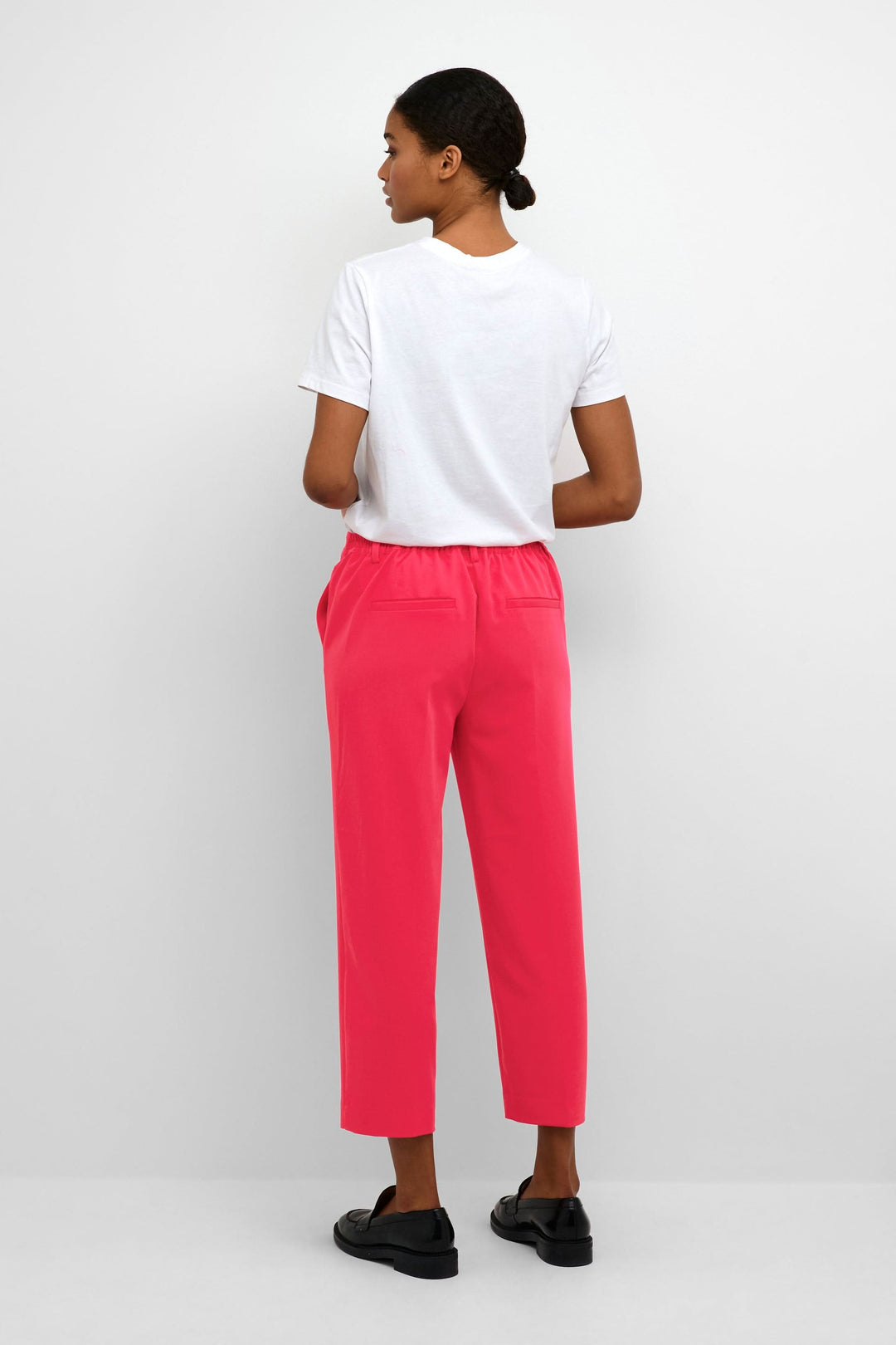 Femme vue de dos portant un pantalon court rose et un t-shirt blanc, avec des poches arrière.