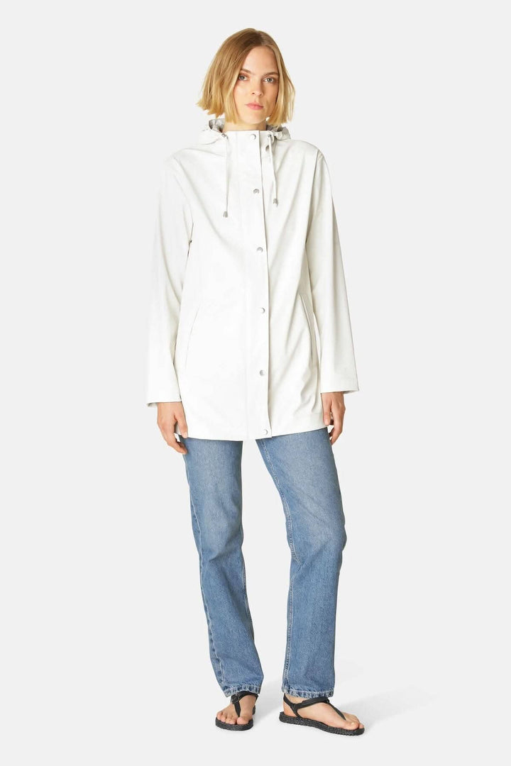 Femme portant un imperméable à coupe droite blanc, tissu léger, avec capuche et jeans.
