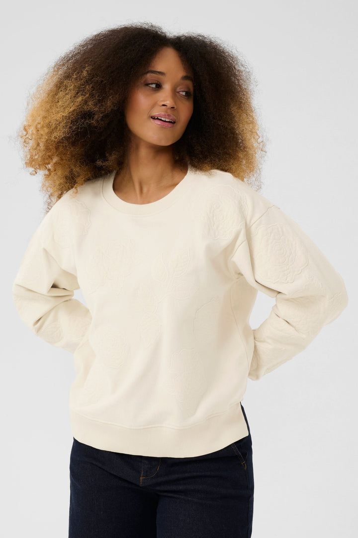 Coton ouaté Josie beige avec broderies florales, confortable et élégant, porté avec un pantalon en jean.