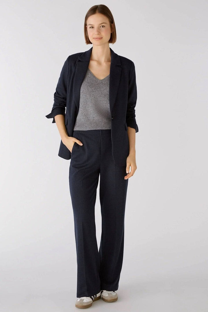 Femme portant un pantalon droit à fines rayures gris marine avec veste assortie et t-shirt gris.