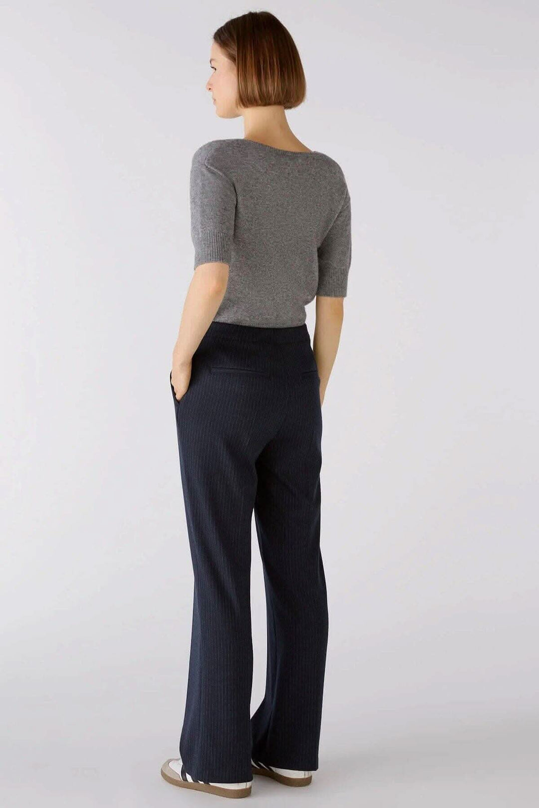 Femme de dos portant un pantalon droit à fines rayures grises et une blouse grise, style contemporain.