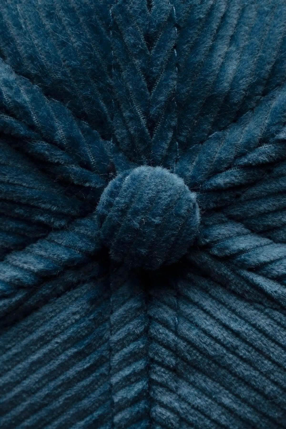 Détail en gros plan d'une casquette en velours côtelé bleu teal, montrant la texture et le bouton central.