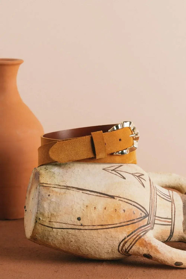 Ceinture Okinawa en cuir velours avec boucle dorée, posée sur une sculpture décorative.