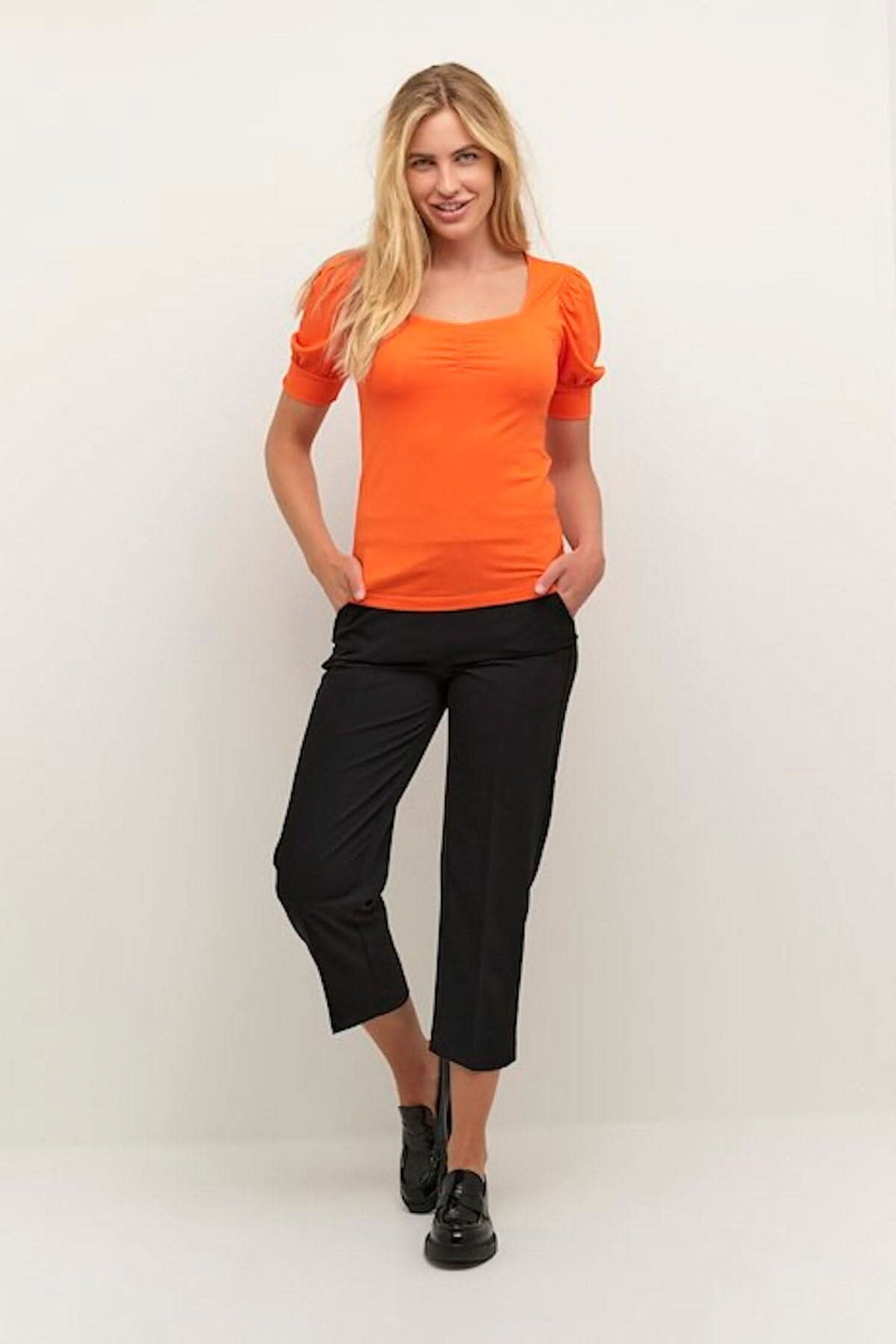 Chandail Silvi orange avec manches ballons, encolure carrée, porté avec un pantalon noir.