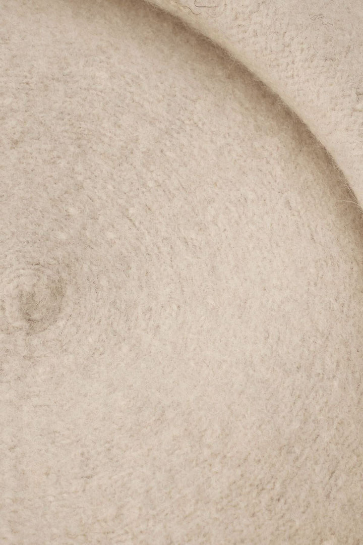 Détails texturés d'un béret en laine doux de couleur beige, mettant en valeur sa finition élégante.