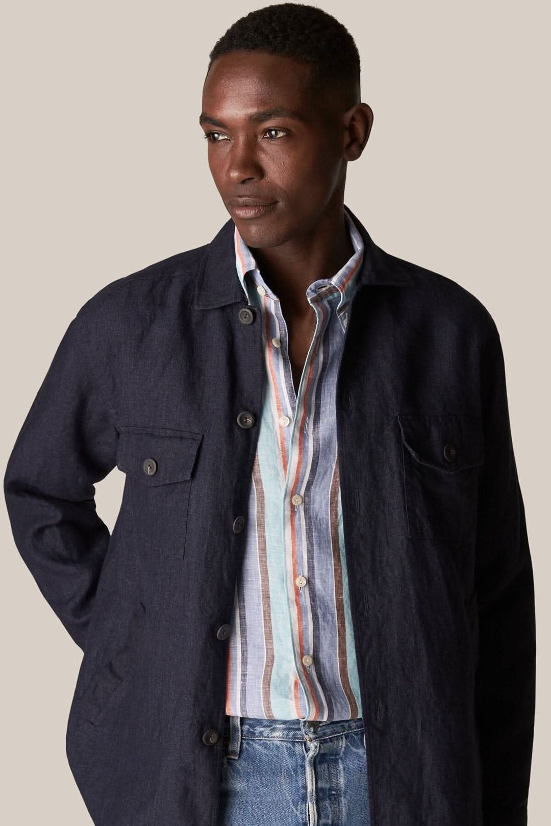 Homme portant une chemise en lin multi-rayures avec une veste noire, style décontracté et moderne.