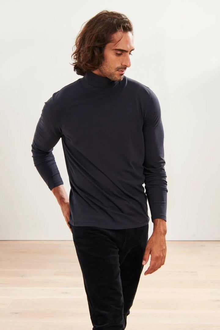 Homme portant un col roulé stretch en coton pima, couleur foncée, dans un intérieur moderne.