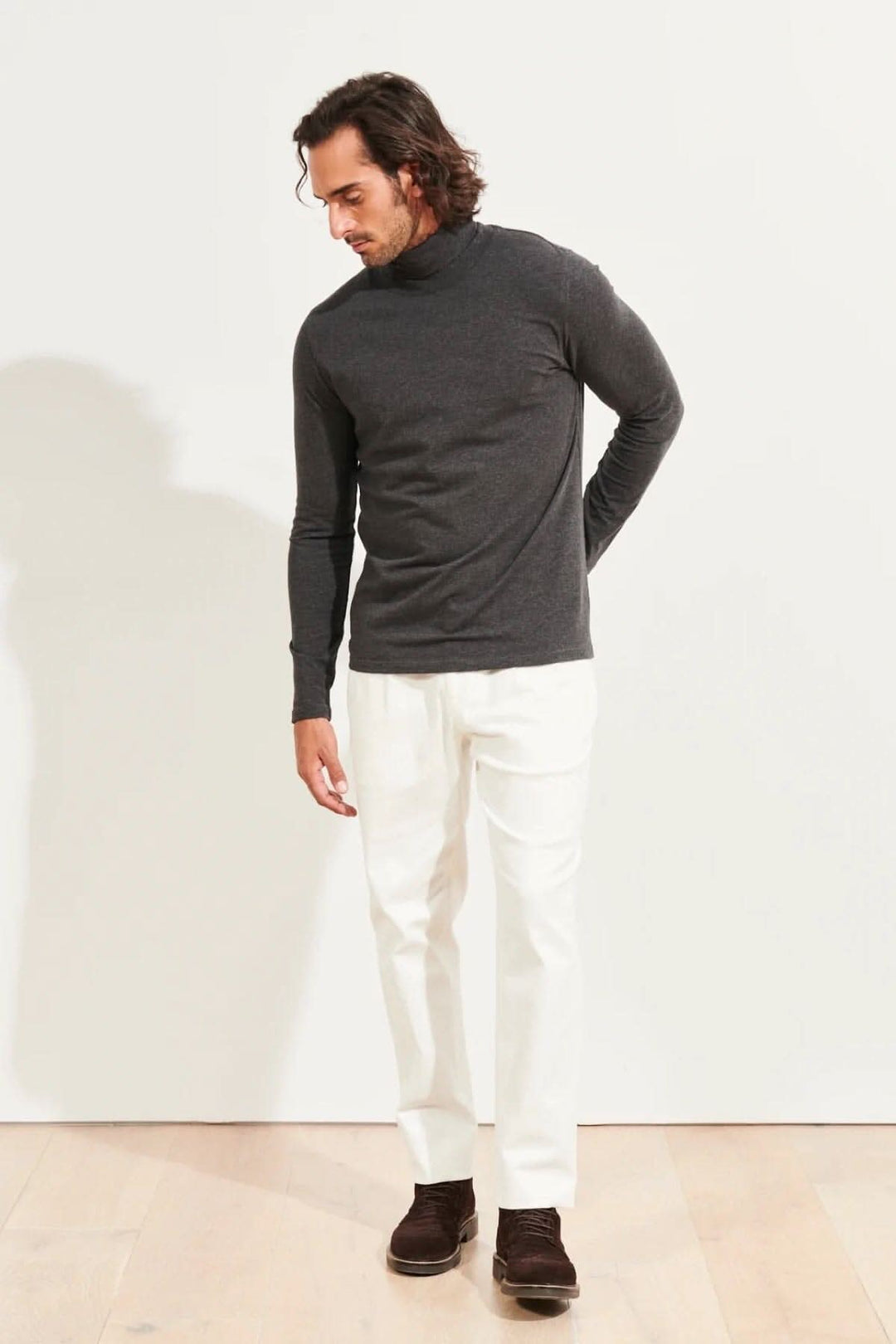 Homme portant un col roulé en coton pima gris avec un pantalon blanc, dans un environnement minimaliste.